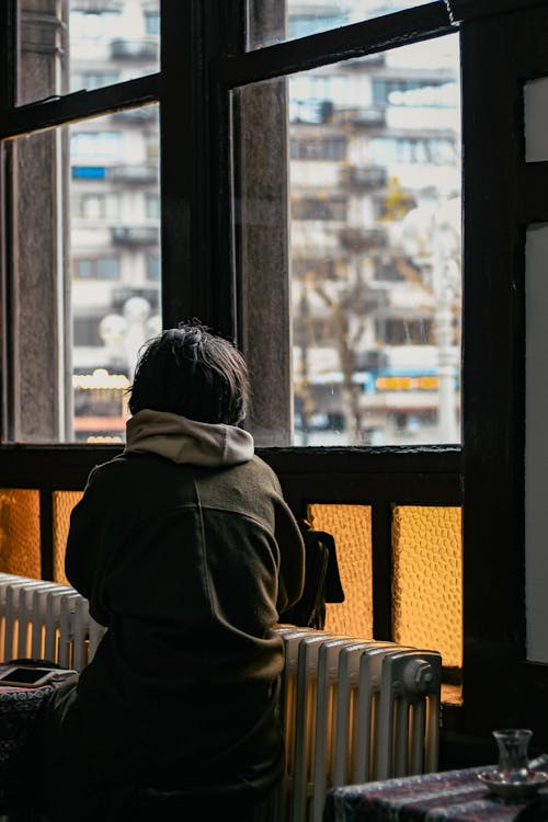 Person in Brown Hoodie Looking at the Window