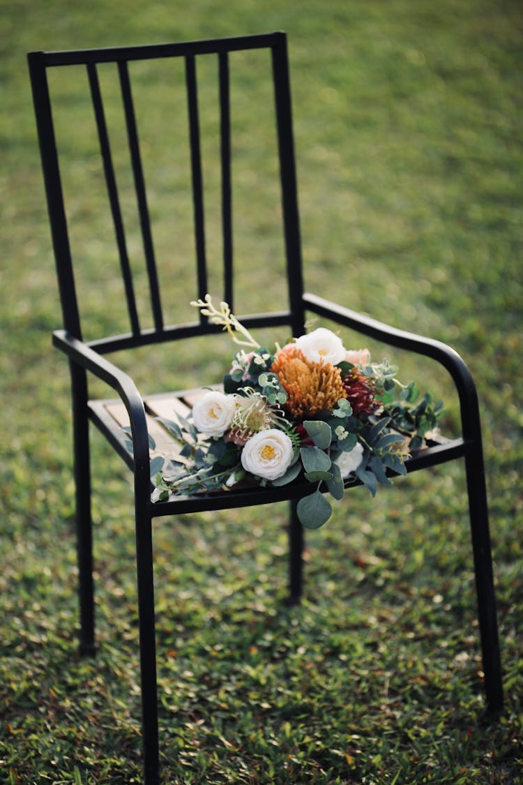 Bunch Of Flowers Laying On Black Metallic Chair Standing On Lawn