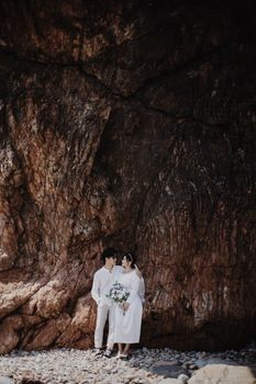 Couple in love posing in white wedding attire near rock formation in Qui Nhơn, Vietnam.