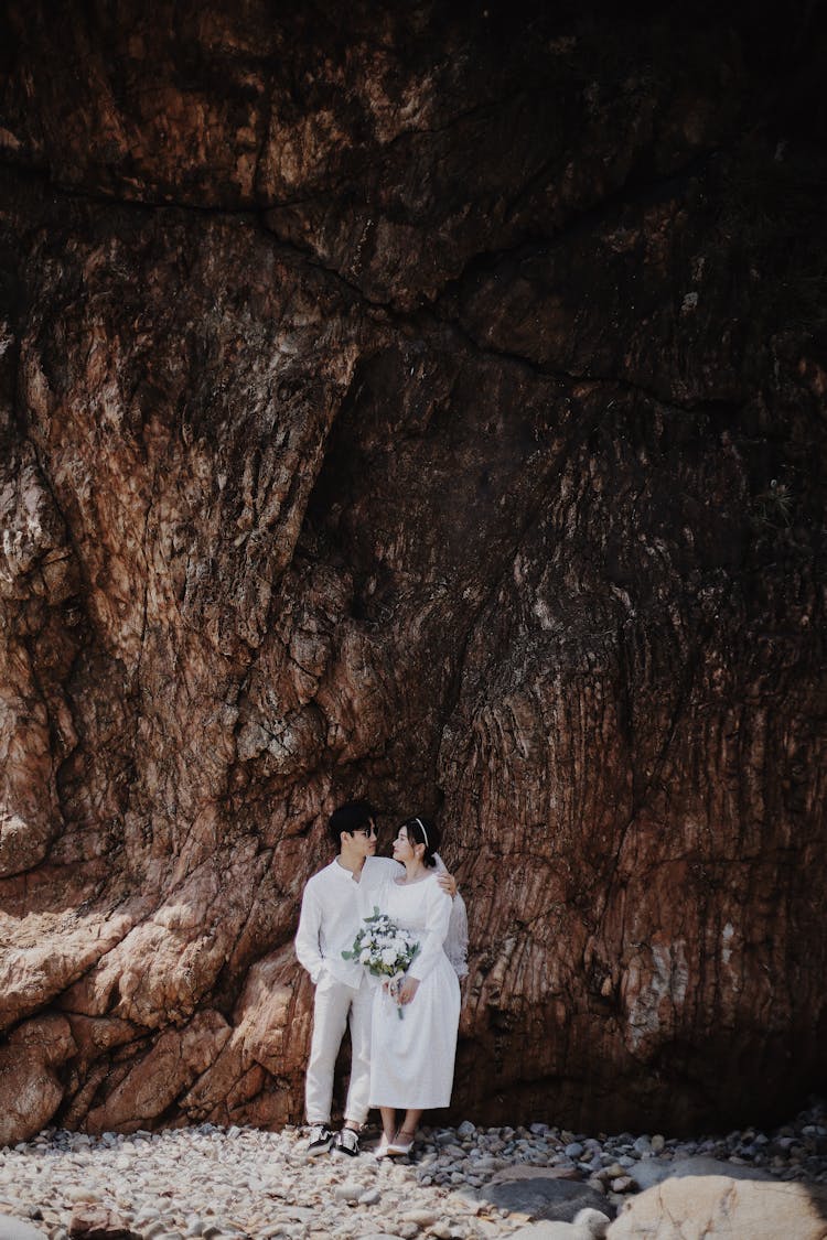 Prewedding Photograph Of Young Couple In White Clothes Under Picturesque Rock