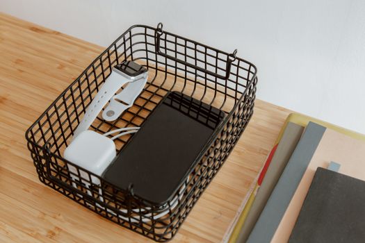 Organized workspace with tech gadgets in a wire basket on a wooden desk.