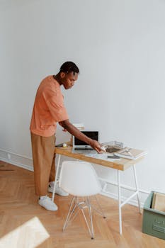 A man standing at a desk organizing papers and electronic devices in a modern office setting.