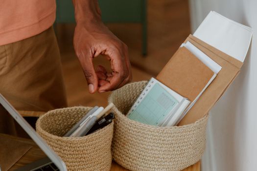 A hand reaching for stationery items in woven baskets on a desk.