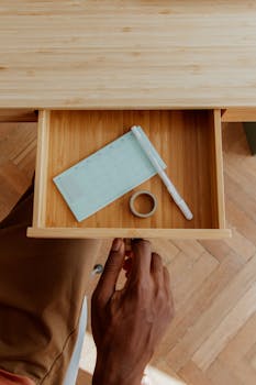 Top view of a man's hand opening a desk drawer with pen, notepad, and tape.