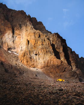 A vibrant yellow tent sits at the base of a rocky mountain in Mtskheta-Mtianeti, Georgia during sunset.