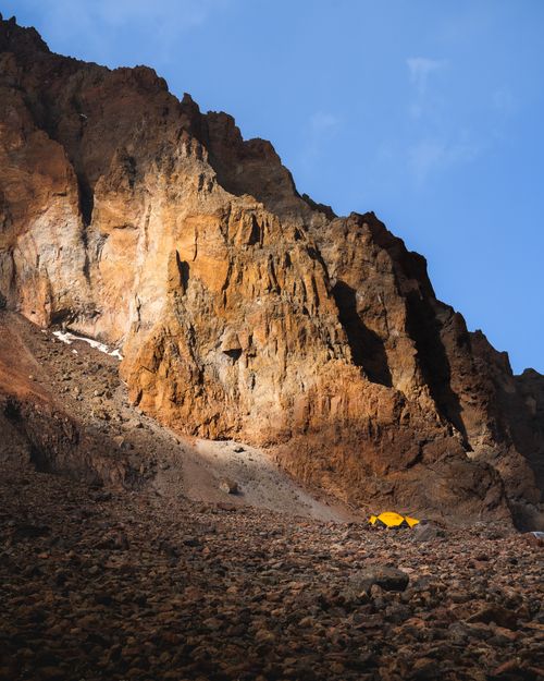 Free A vibrant yellow tent sits at the base of a rocky mountain in Mtskheta-Mtianeti, Georgia during sunset. Stock Photo