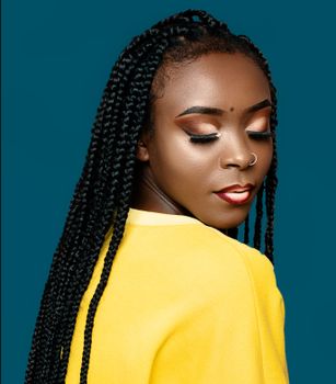Close-up portrait of a woman with braided hair and bold makeup against a blue background.