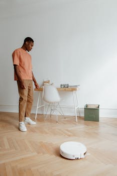 Man in casual attire looking at robot vacuum in a modern home office setting.