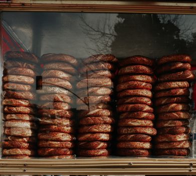 Stacks of fresh bagels with sesame seeds displayed in a bakery glass window.