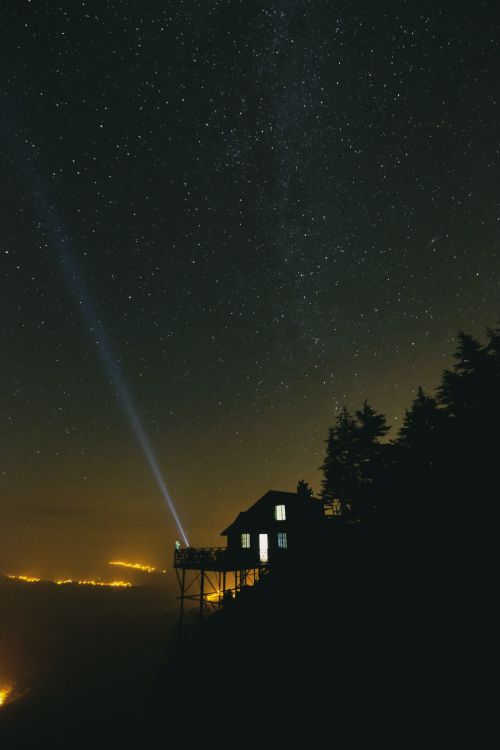 Free Dramatic starlit sky with a cabin silhouette and a beam of light on a clear night. Stock Photo