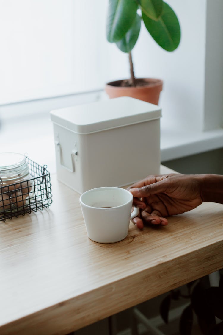 Hand Holding Cup And Box On Table