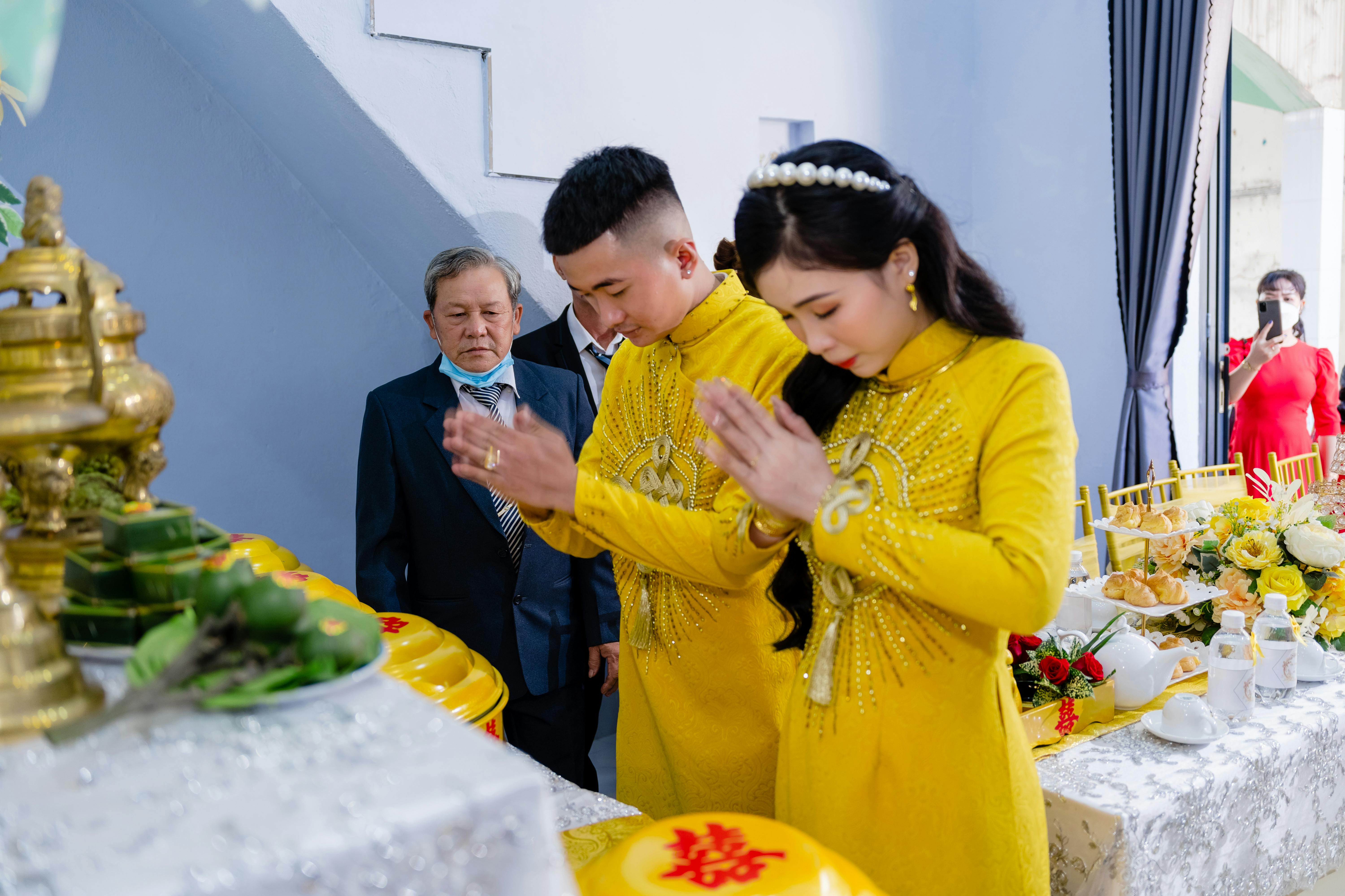 A traditional Vietnamese couple in yellow attire engaged in a wedding ceremony ritual indoors.