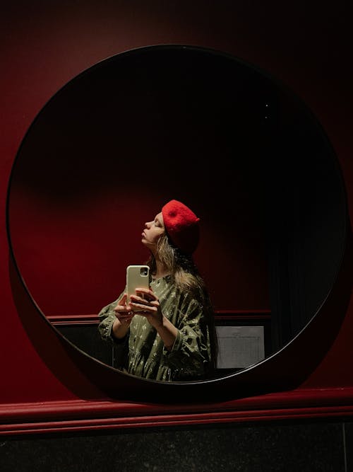 A Woman in Red Beret Cap Taking Picture in Front of the Mirror