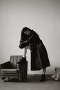 Woman with Long Black Hair in Leather Coat Standing with One Leg on Armchair
