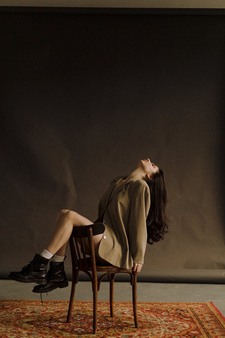 Woman With Long Black Hair Sitting In Chair With Tilt Head And Legs On Backrest