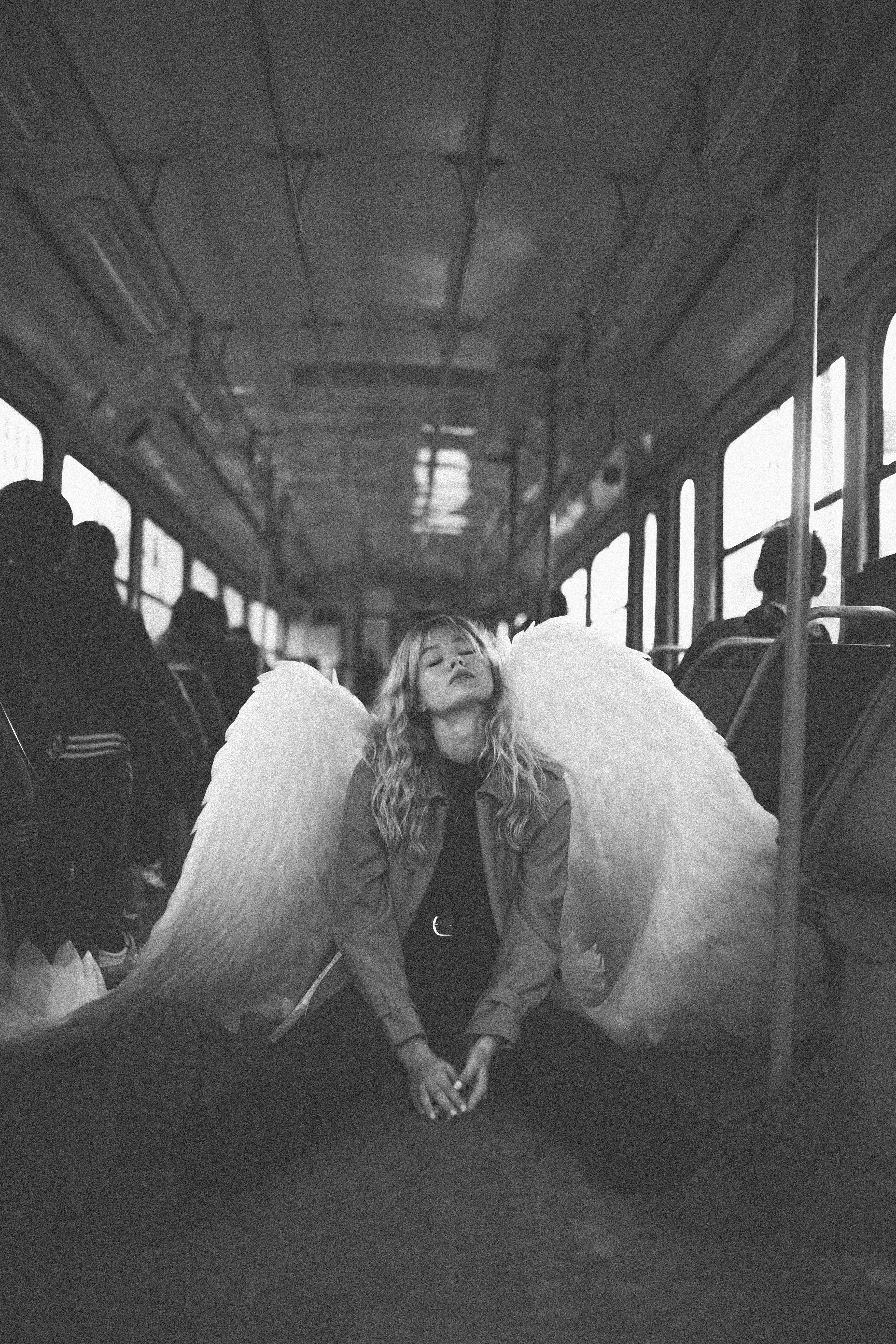 young blond woman disguised as angel kneeling on bus with hands clasped