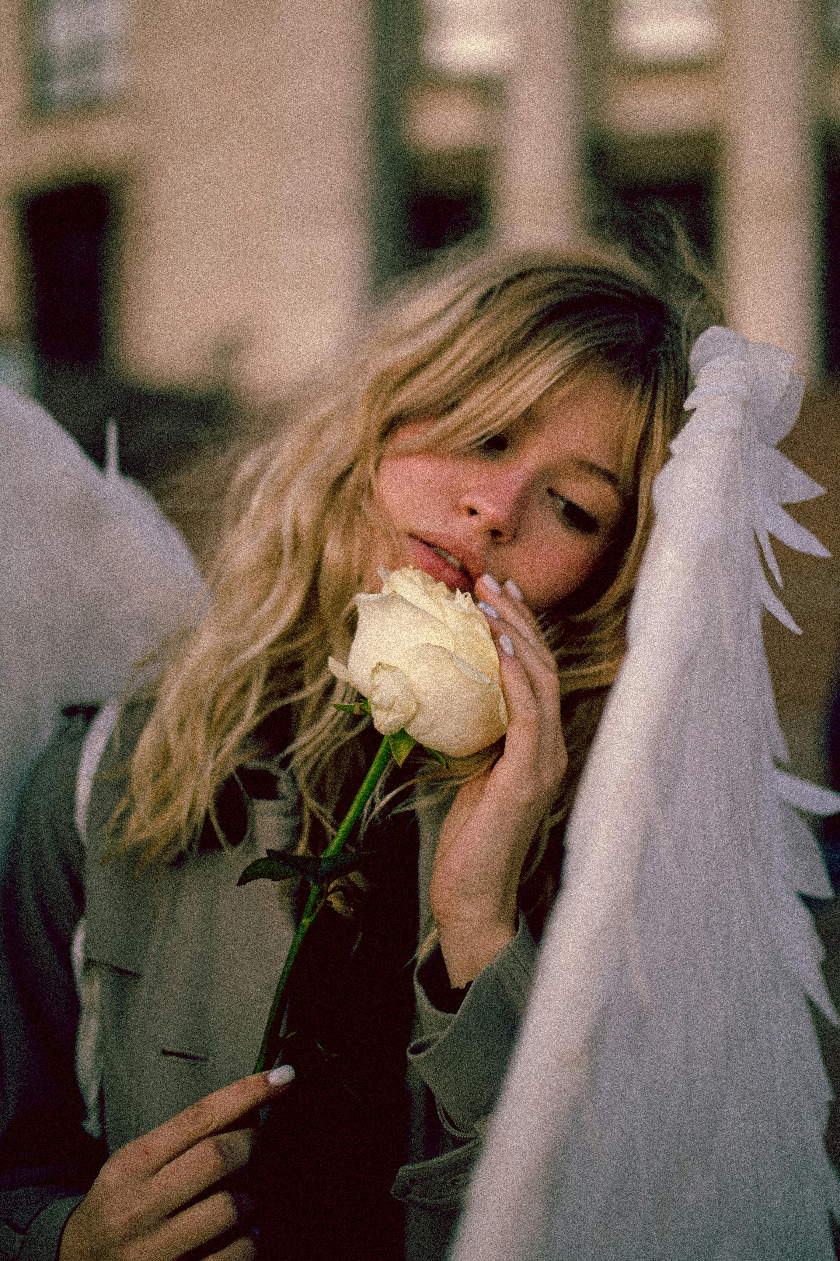 blond woman with angel wings holding white rose and touching flower