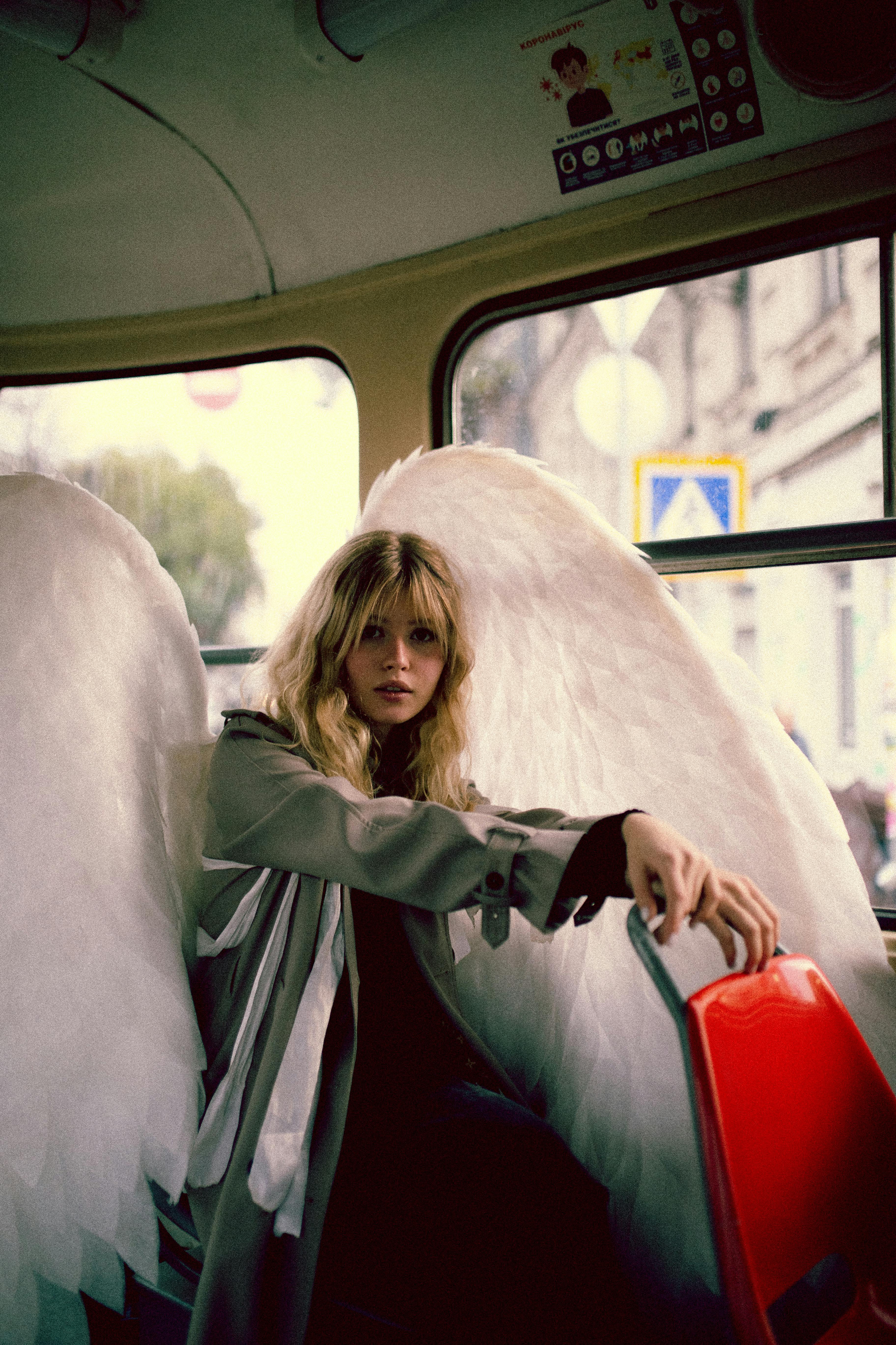 blond woman in coat and with angel wings sitting in city bus