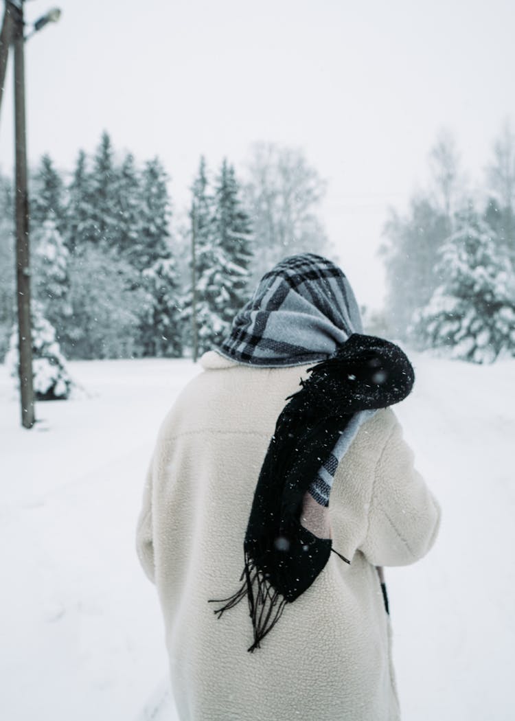 A Back View Of A Person In Winter Clothes Walking On A Snow Covered Ground