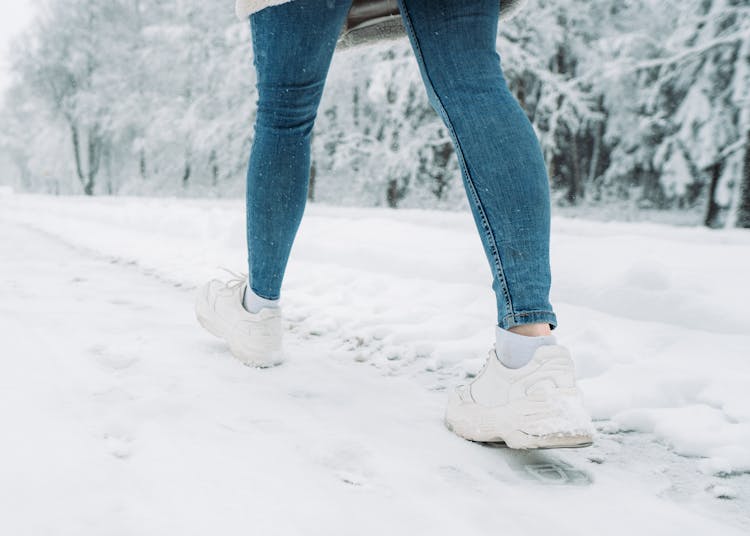 A Person In Denim Jeans And White Shoes Walking On A Snow Covered Ground