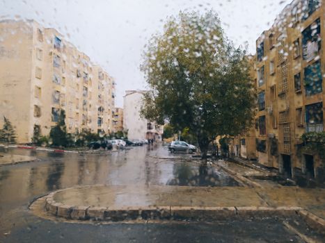 Raindrops on window obscuring a city street view, highlighting urban weather.