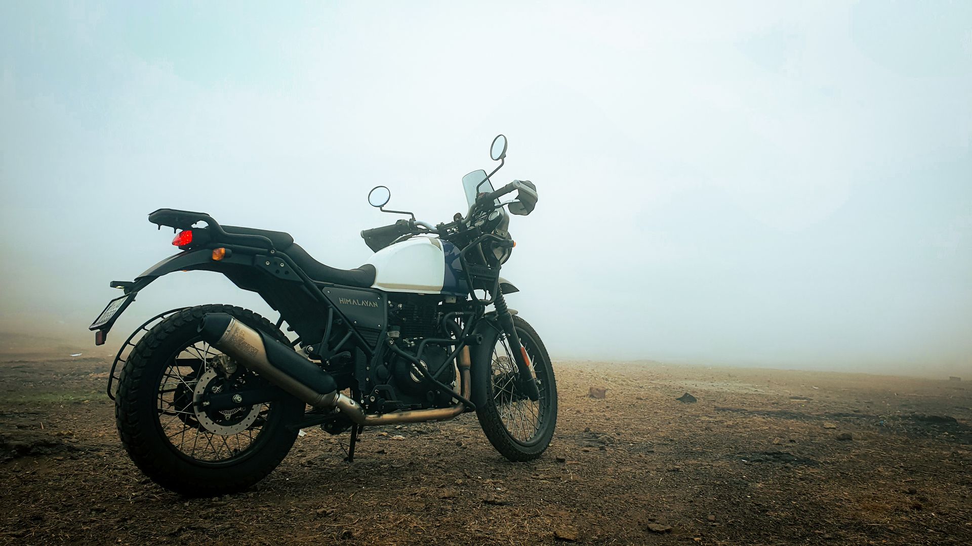 A Royal Enfield Himalayan motorcycle parked on a misty dirt road, exuding adventure vibes.