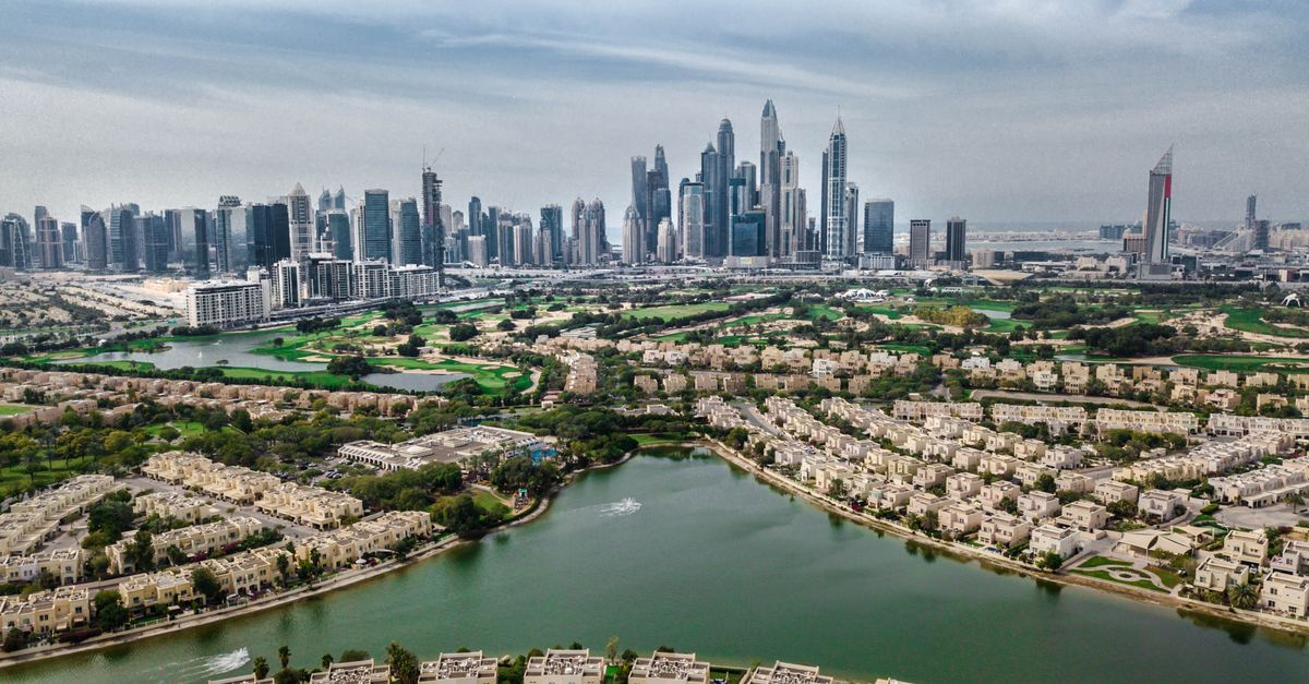 High-rise buildings of Dubai's skyline above residential areas with lush greenery and water.