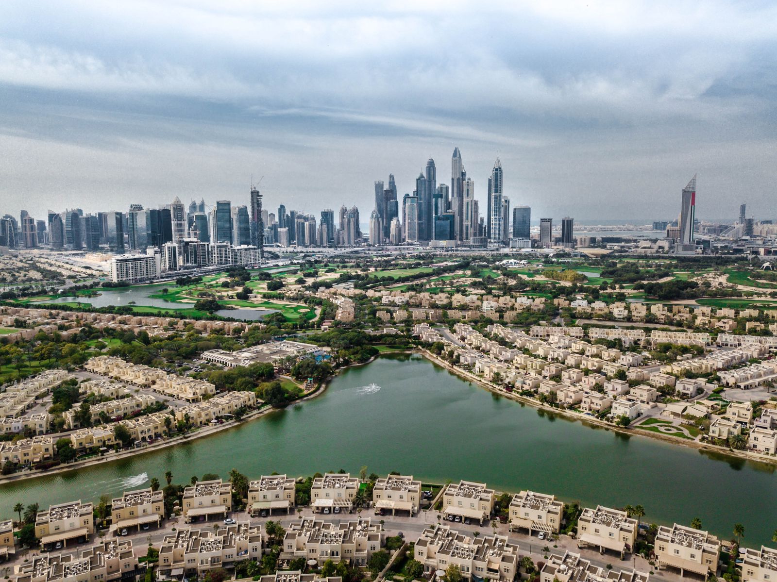 Aerial view of a leafy low-rise Dubai community set around a lake beside the golf course, the skyline beyond