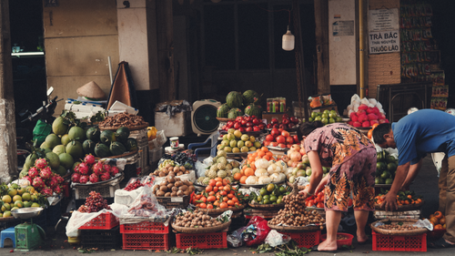 Free Vibrant street market featuring fresh fruits with two vendors arranging the display. Stock Photo