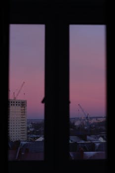 Silhouette of construction cranes seen through a window during a captivating purple sunset.