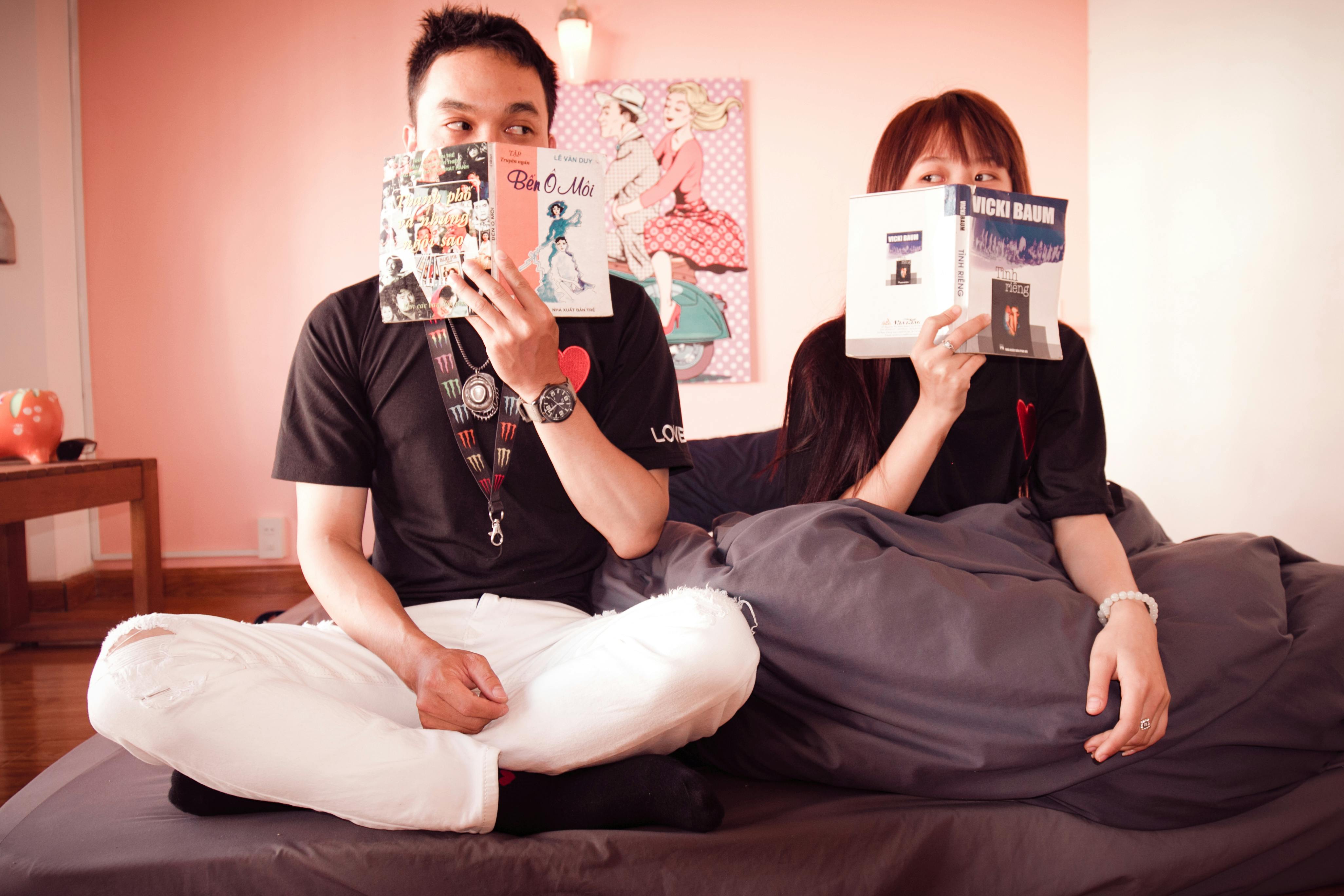 Couple holding books sitting on bed | Photo: Pexels