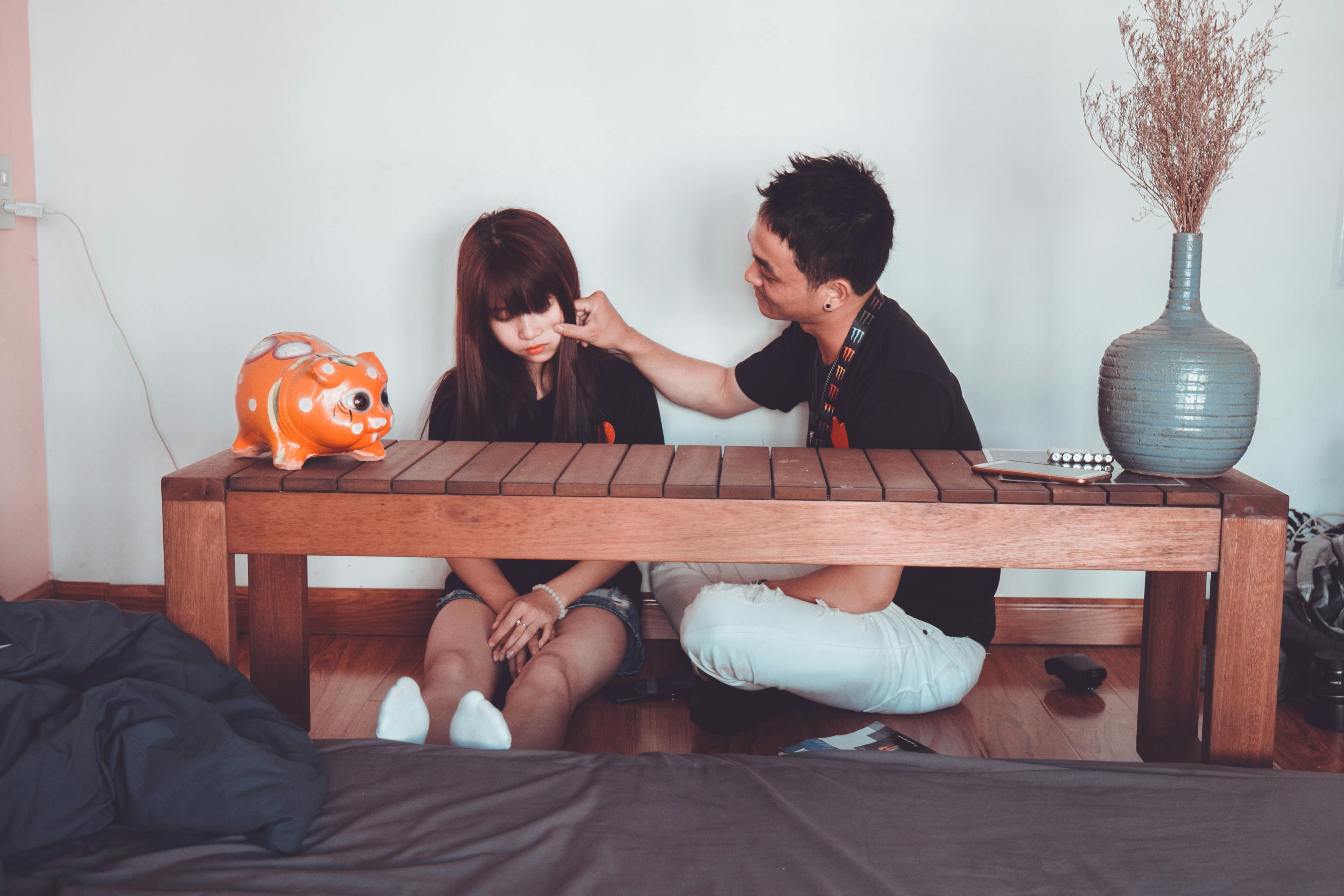 Man Pinching the Cheek of Woman Sitting Near Rectangular Brown Wooden Coffee Table
