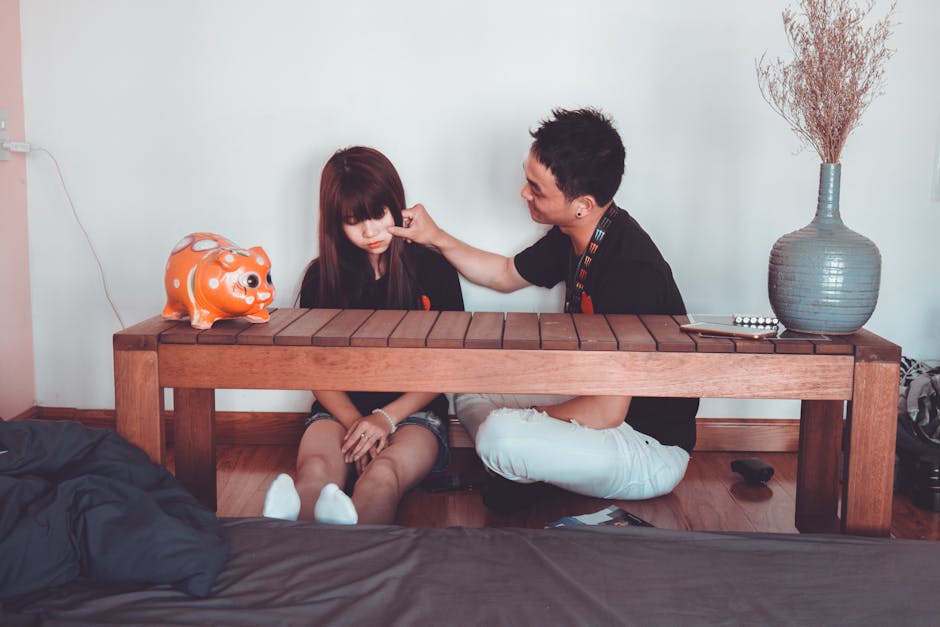 Man Pinching the Cheek of Woman Sitting Near Rectangular Brown Wooden Coffee Table