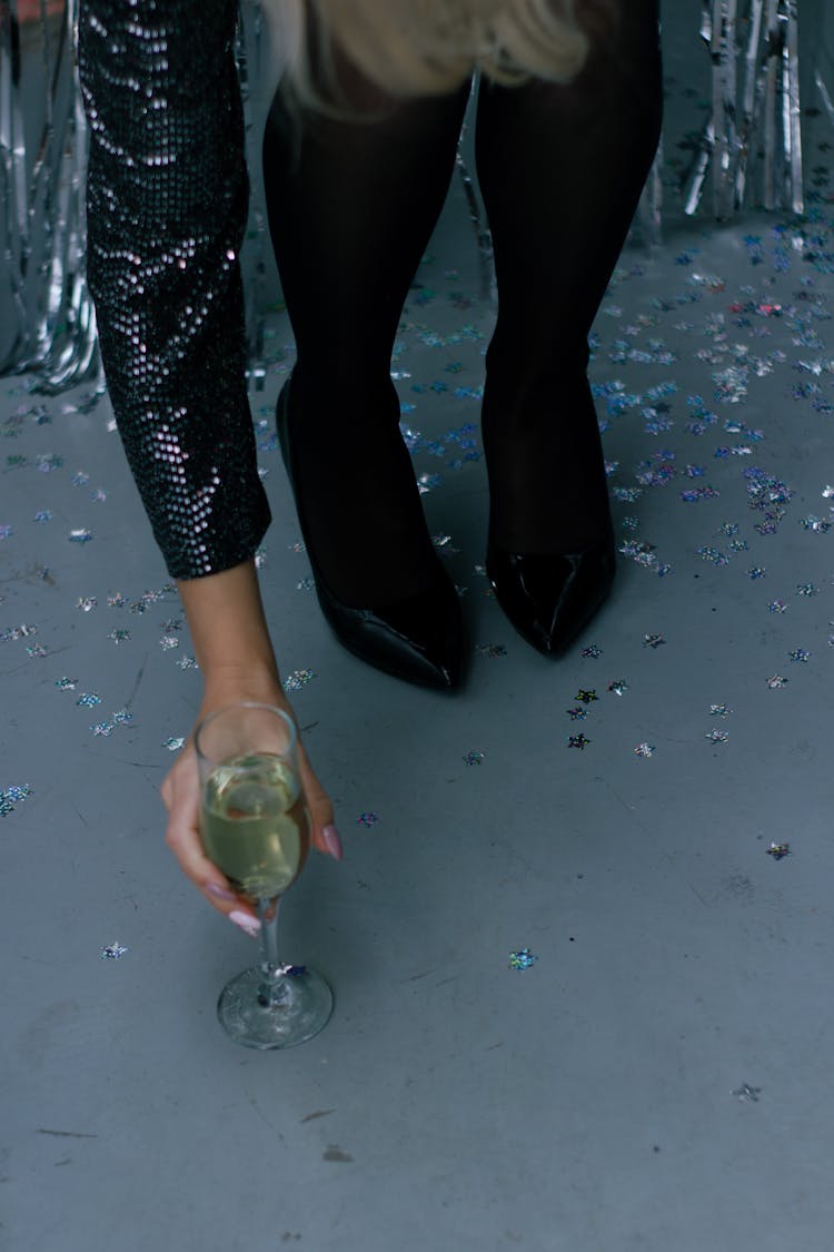 A Person Wearing Black Heels Getting The Glass Of Champagne On The Floor
