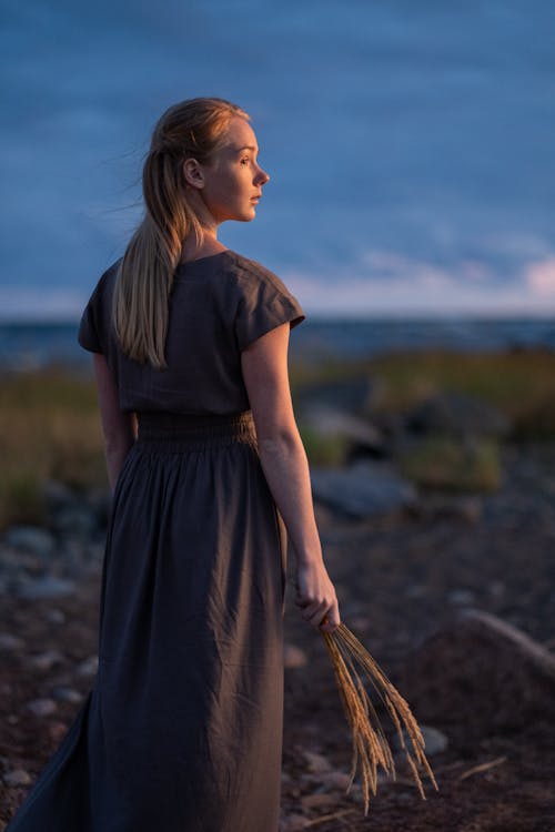 A Woman in Gray Dress Standing while Holding a Wheat Grass