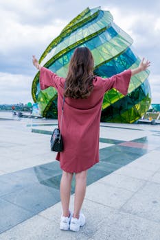 Back view of a joyful woman in a pink dress at a modern green landmark.