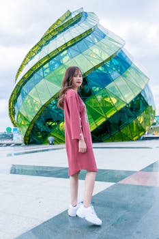 Asian woman elegantly posing in front of modern glass architecture outdoors.