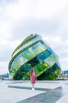 Asian woman standing at a distinctive green glass landmark on a sunny day, perfect for travel themes.