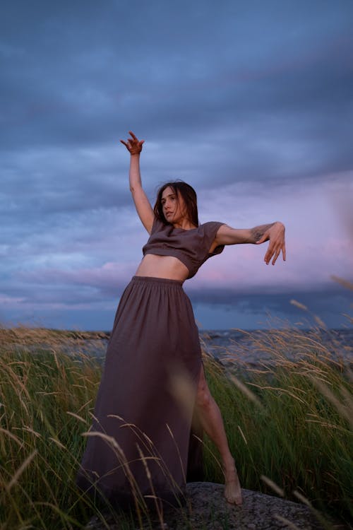 Woman in Brown Dress Dancing on a Grass Field