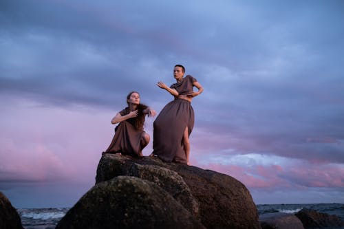 Women in Brown Dress Dancing on Brown Rock on a Shore