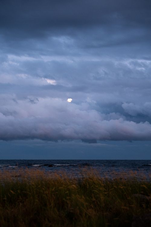 Free A scenic view of the ocean under a cloudy sky with a visible moon, perfect for wallpapers. Stock Photo