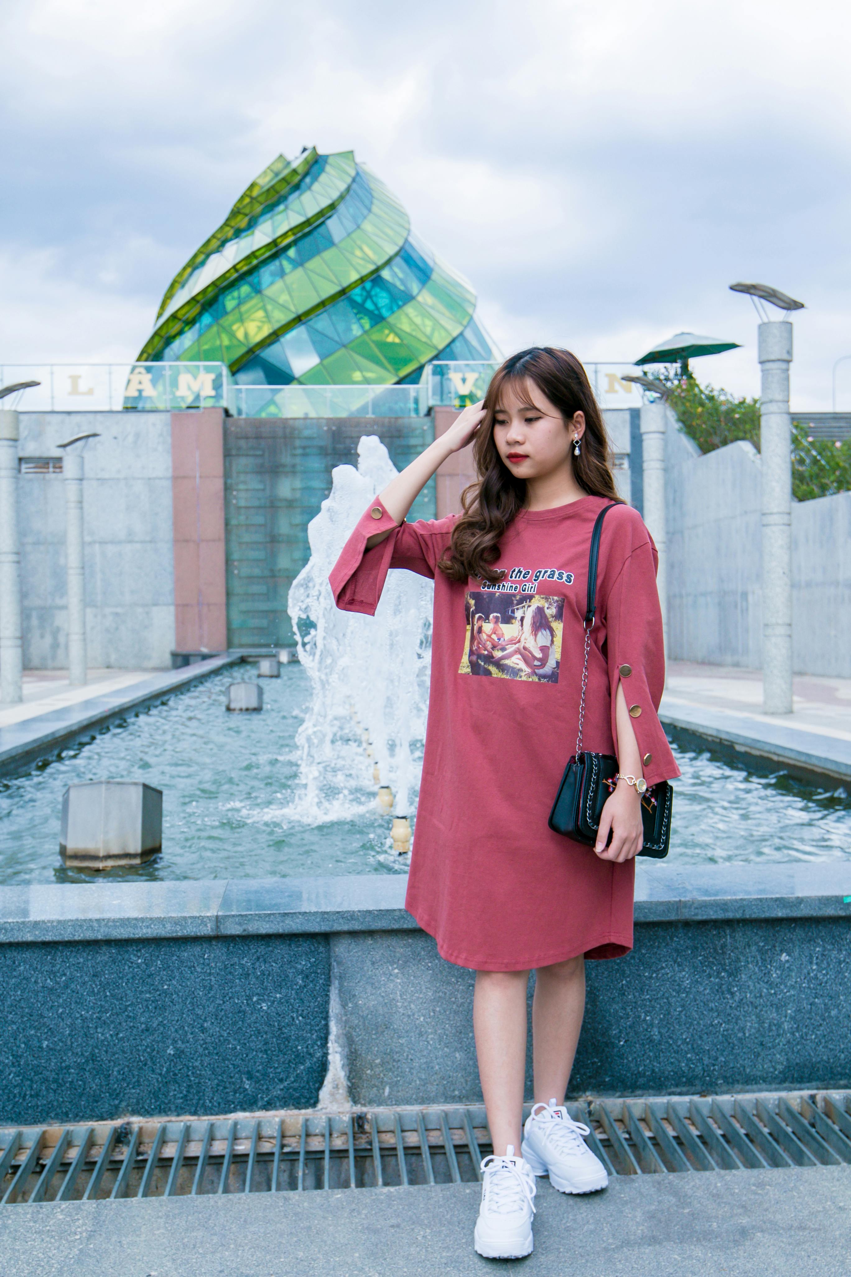 Woman Wearing Maroon Crew-neck Long-sleeved Dress Standing Next to Fountain Under Cloudy Sky ...