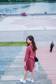 一位时尚的年轻女子穿着红色连衣裙，从风景秀丽的海滨楼梯上走下来