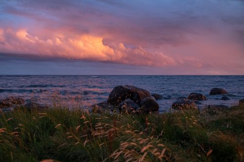 Free Breathtaking view of a sunset over the sea with vibrant clouds and rocky shoreline. Stock Photo