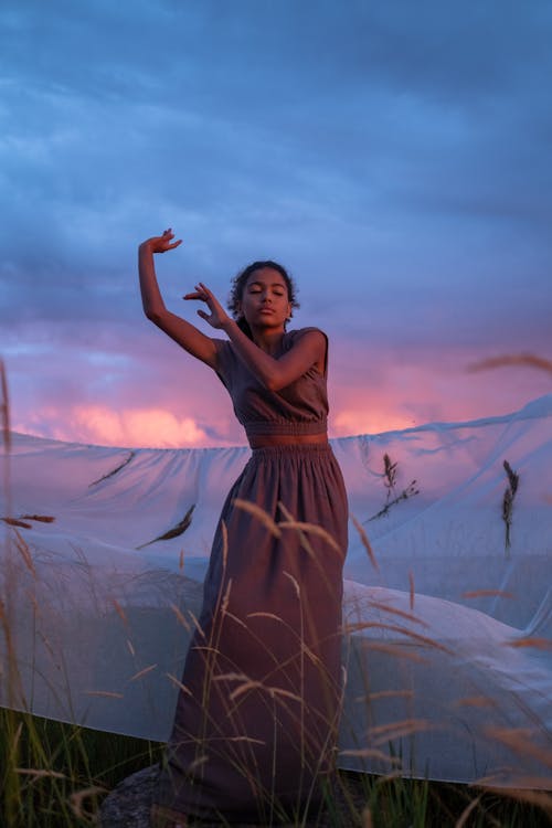 A Woman in Brown Dress Dancing Beside a Net and Brown Grass 