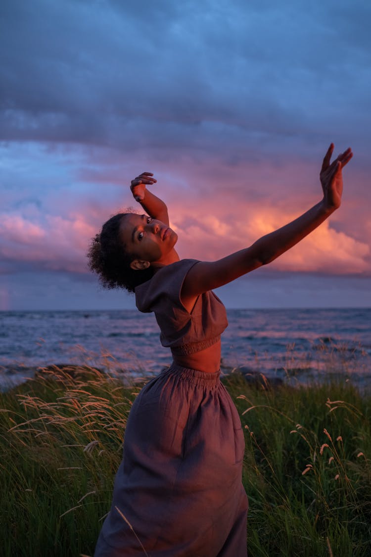 A Young Woman In A Brown Dress Dancing By The Seaside