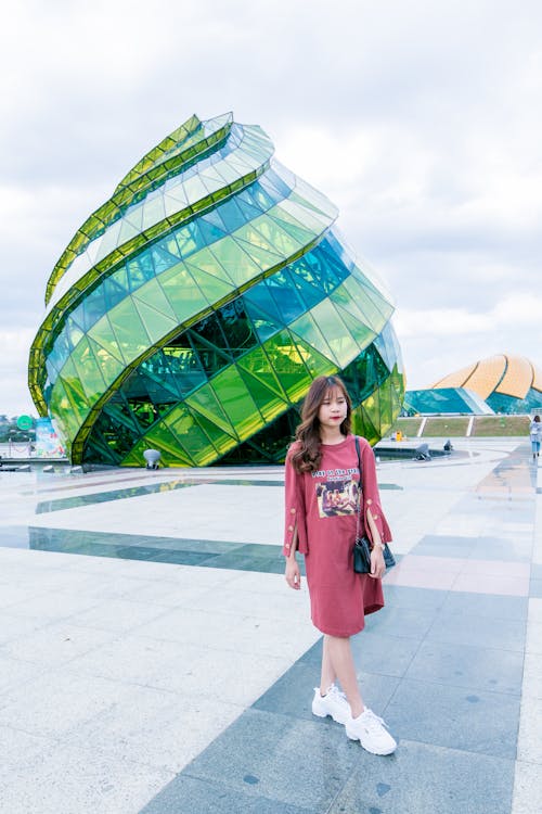 Free Woman in Red Long-sleeved Top Wearing White Sneakers Walking in Front of Green and Blue Glass Building Stock Photo