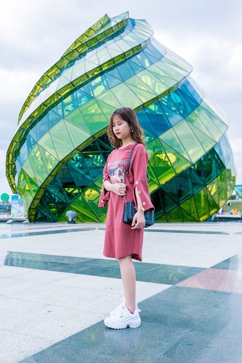 Free Girl Wearing Red Long-sleeved Dress and White Low-top Shoes Standing Near Green Glass Structure Stock Photo