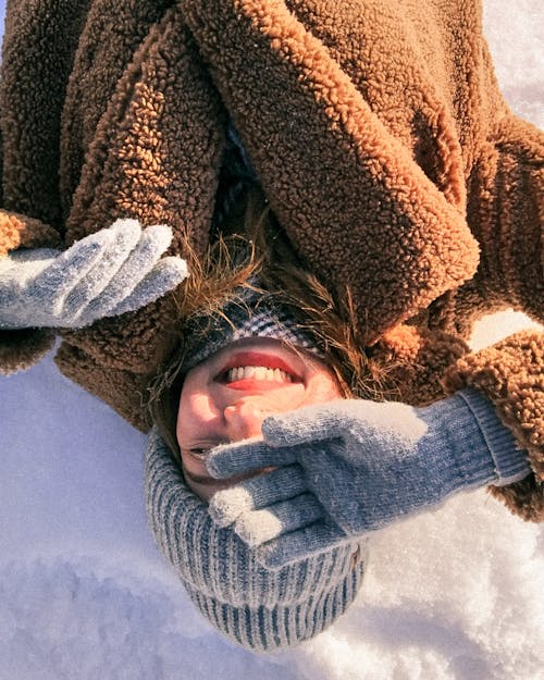 Free Woman in Brown and White Sweater Smiling while Lying on a Snow Covered Ground Stock Photo