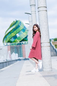 Young woman poses by pillars with modern architecture in the background.